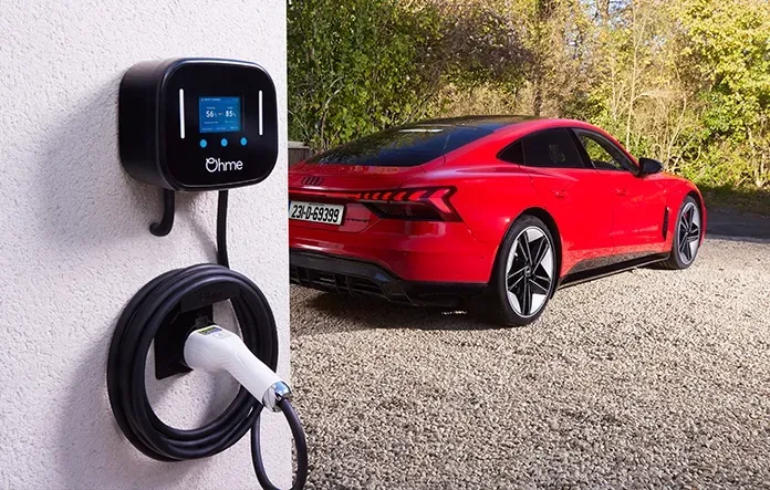 Ohme Home Pro EV charger mounted on a home wall, charging a red Audi e-tron parked on gravel